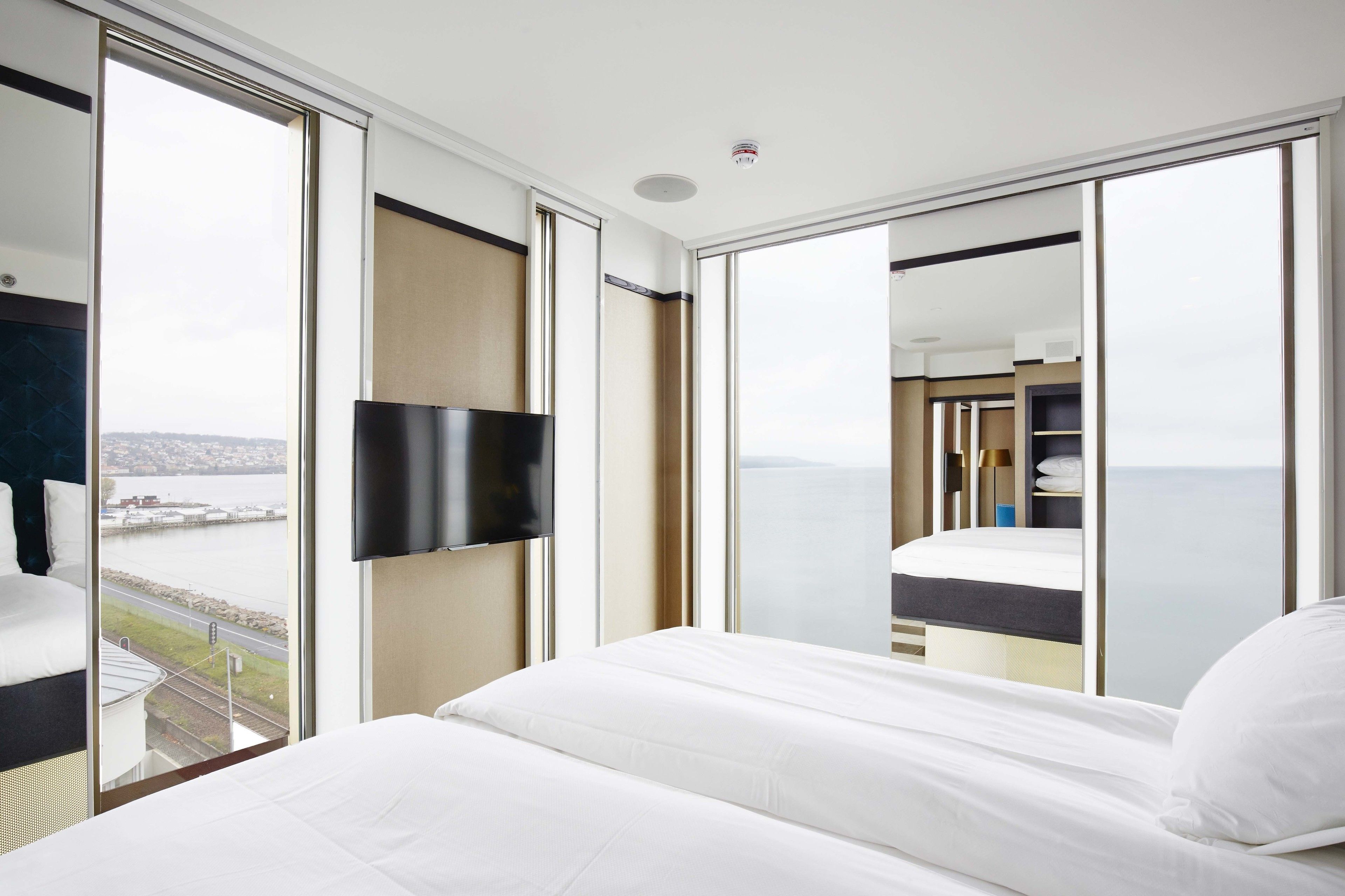 A hotel room with a large bed, a flat-screen TV, and a view of the city and water.