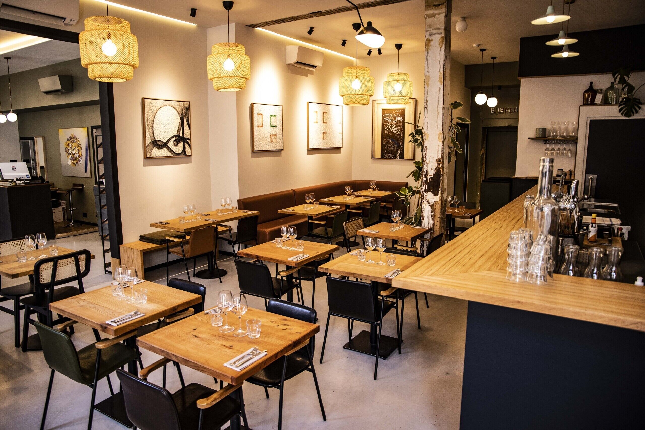 Ein Restaurant mit Holztischen und -stühlen, hängenden Korbtischen und gerahmten Kunstwerken an den Wänden.