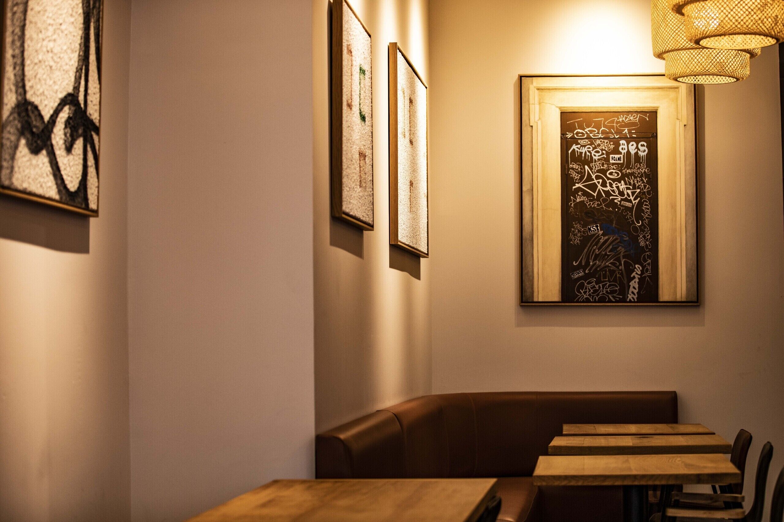 A restaurant interior with a booth seating area, wooden tables, and framed artwork on the walls.