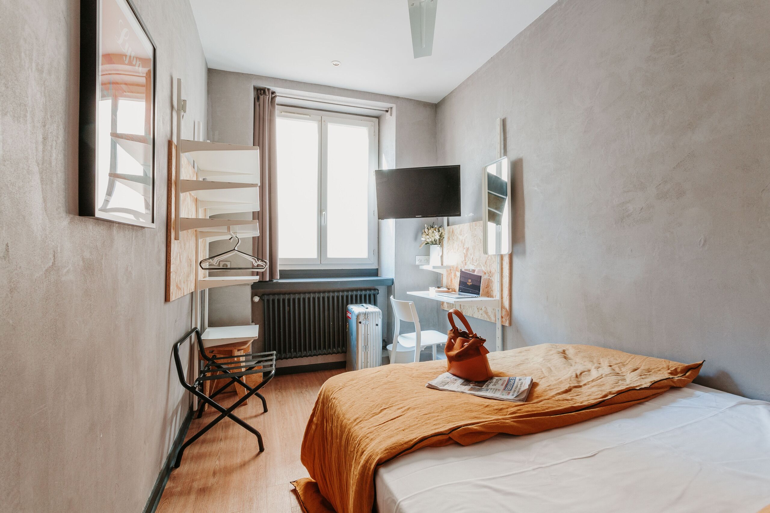 Ein Hotelzimmer mit Bett, Schreibtisch, Stuhl, Heizkörper, Fernseher und einem Fenster mit Vorhängen.