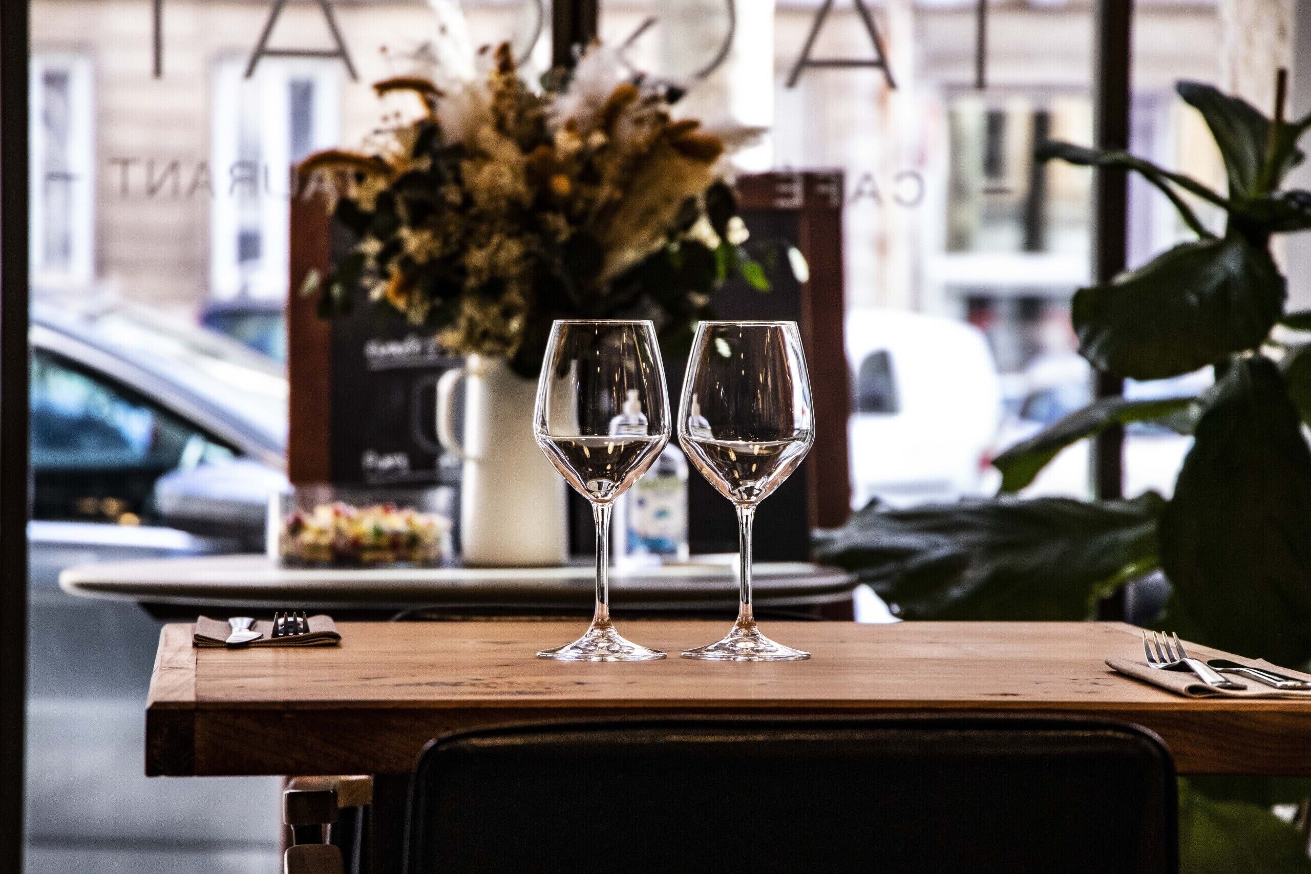 A table with two empty wine glasses and a menu stand with a floral arrangement in the background.