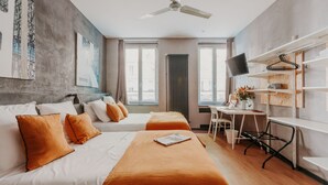 Ein Hotelzimmer mit zwei Betten, einem Schreibtisch, einem Sessel, einem Fernseher und einem Deckenventilator.