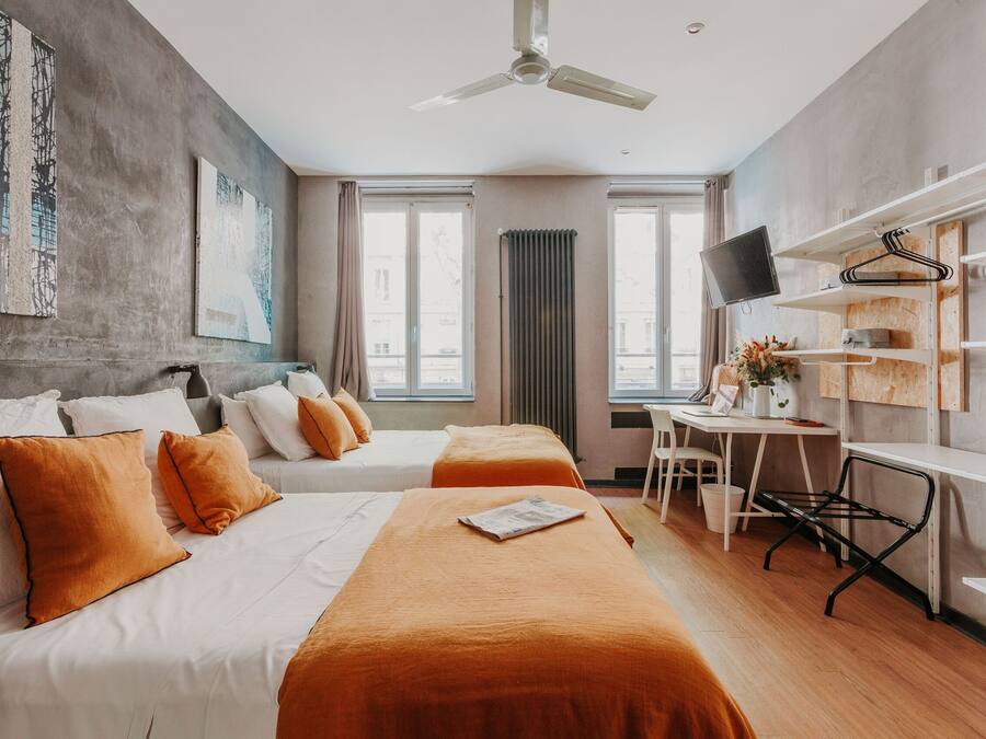 A hotel room with two beds, a desk, a chair, a TV, and a ceiling fan.