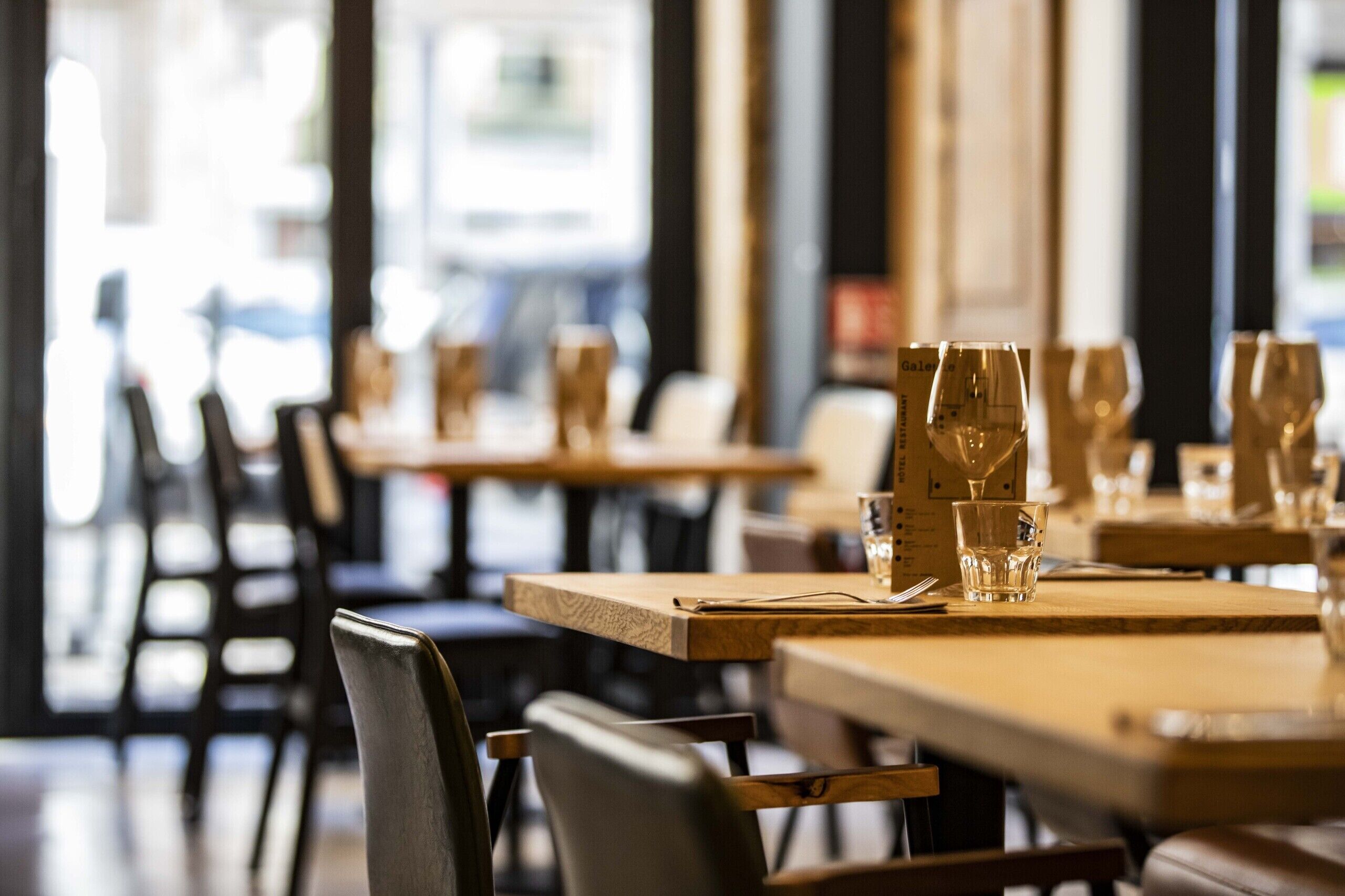 Un interior de restaurante con mesas y sillas de madera, vasos colocados sobre cada mesa y un menú en la mesa.