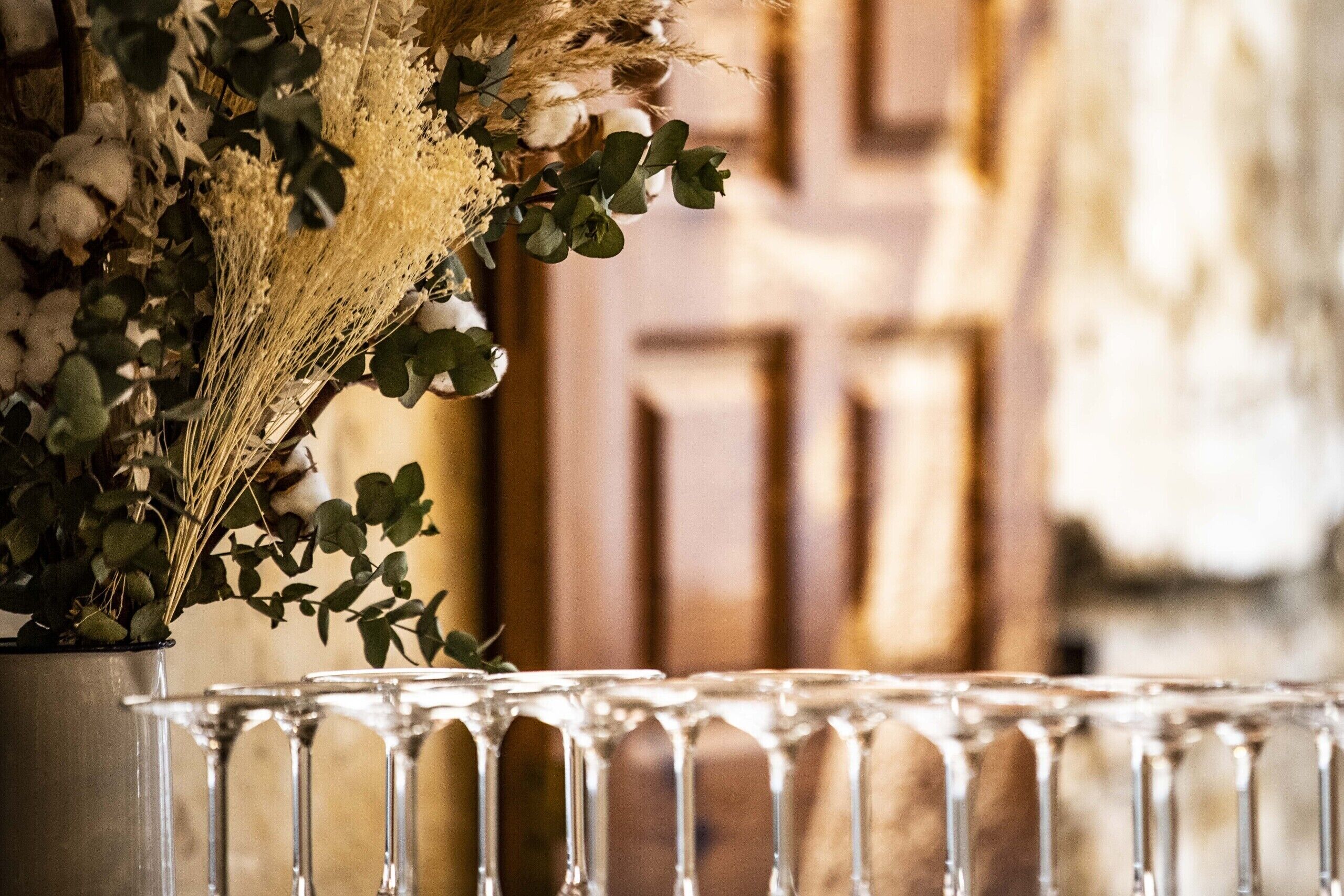 A glass table with a vase of dried flowers and green leaves.