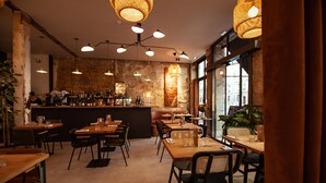 Ein Restaurantinneres mit Holztischen und -stühlen, einer Bar mit Flaschen und großen Fenstern, die für natürliches Licht sorgen.