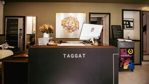 Ein Empfangstresen mit dem Schriftzug "TAGGAT", einem Computer, einer Blumenvase und einem gerahmten Kunstwerk darüber.