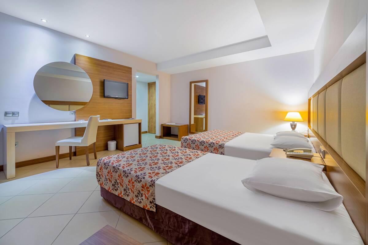 Une chambre d’hôtel avec deux lits, un bureau, une chaise, une télévision et une lampe.