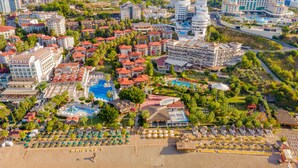 Luchtbeeld van een resort met meerdere gebouwen, een groot zwembad en een strand met ligbedden.