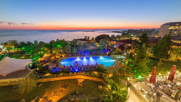 Een resort met een groot zwembad, terras en uitzicht op de oceaan in de schemering.
