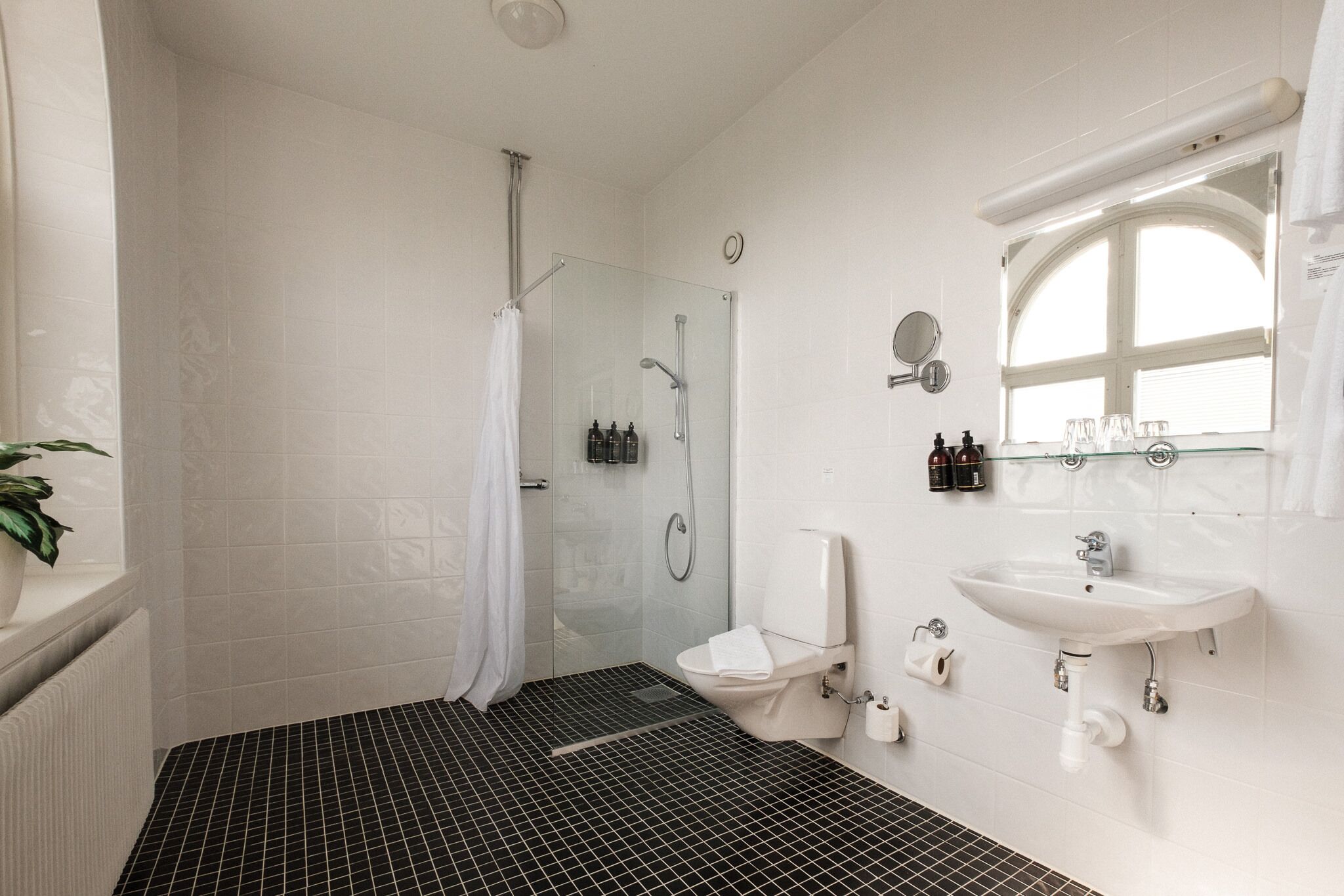Un baño moderno con cabina de ducha de vidrio, un lavabo blanco y un ventanal grande.
