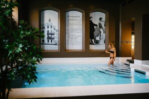 Ein Schwimmbecken mit einer Person im Wasser, umgeben von Infotafeln und einer Pflanze.
