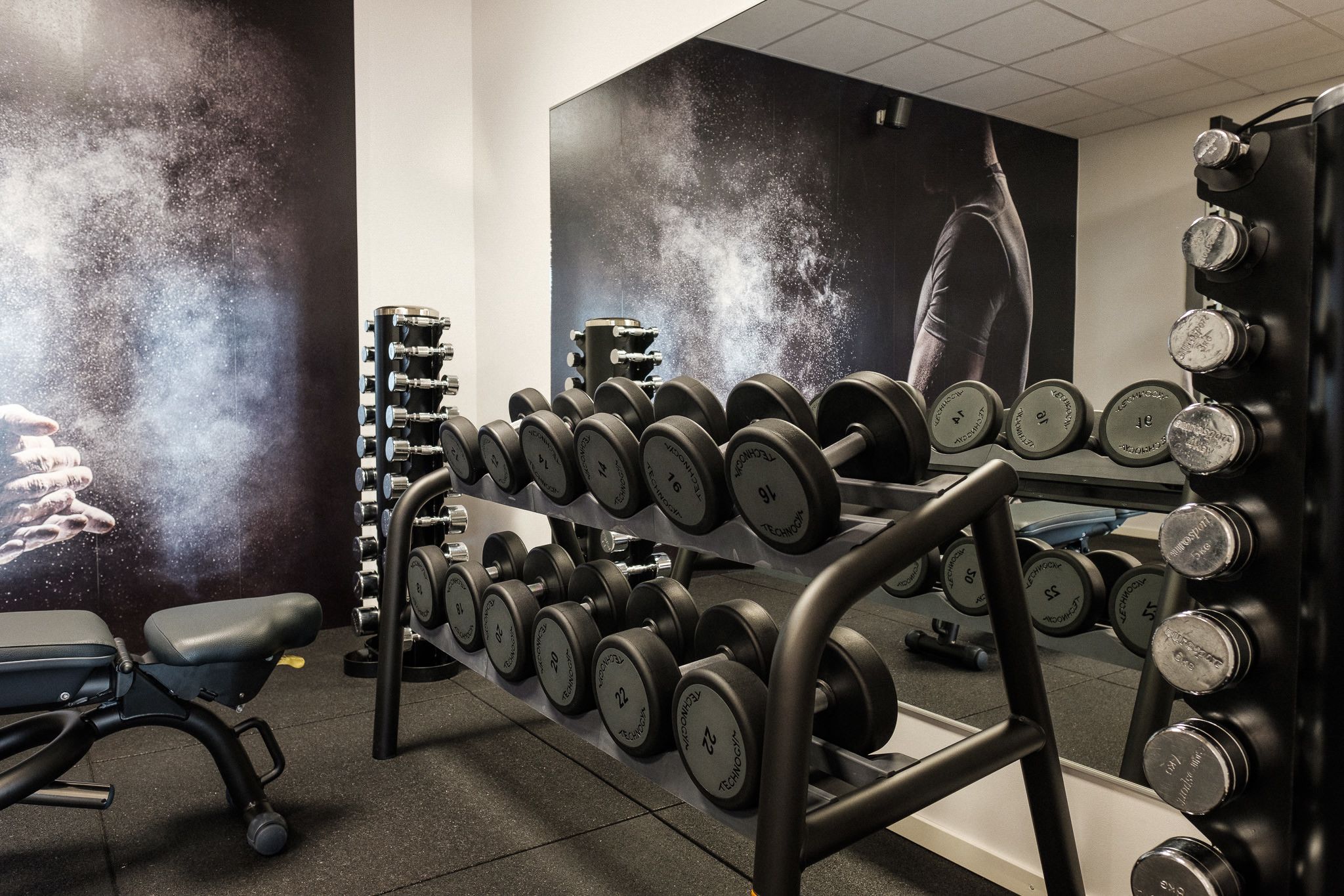 Ein Fitnessraum mit Krafttrainingsgeräten, darunter Kurzhanteln und Langhanteln.