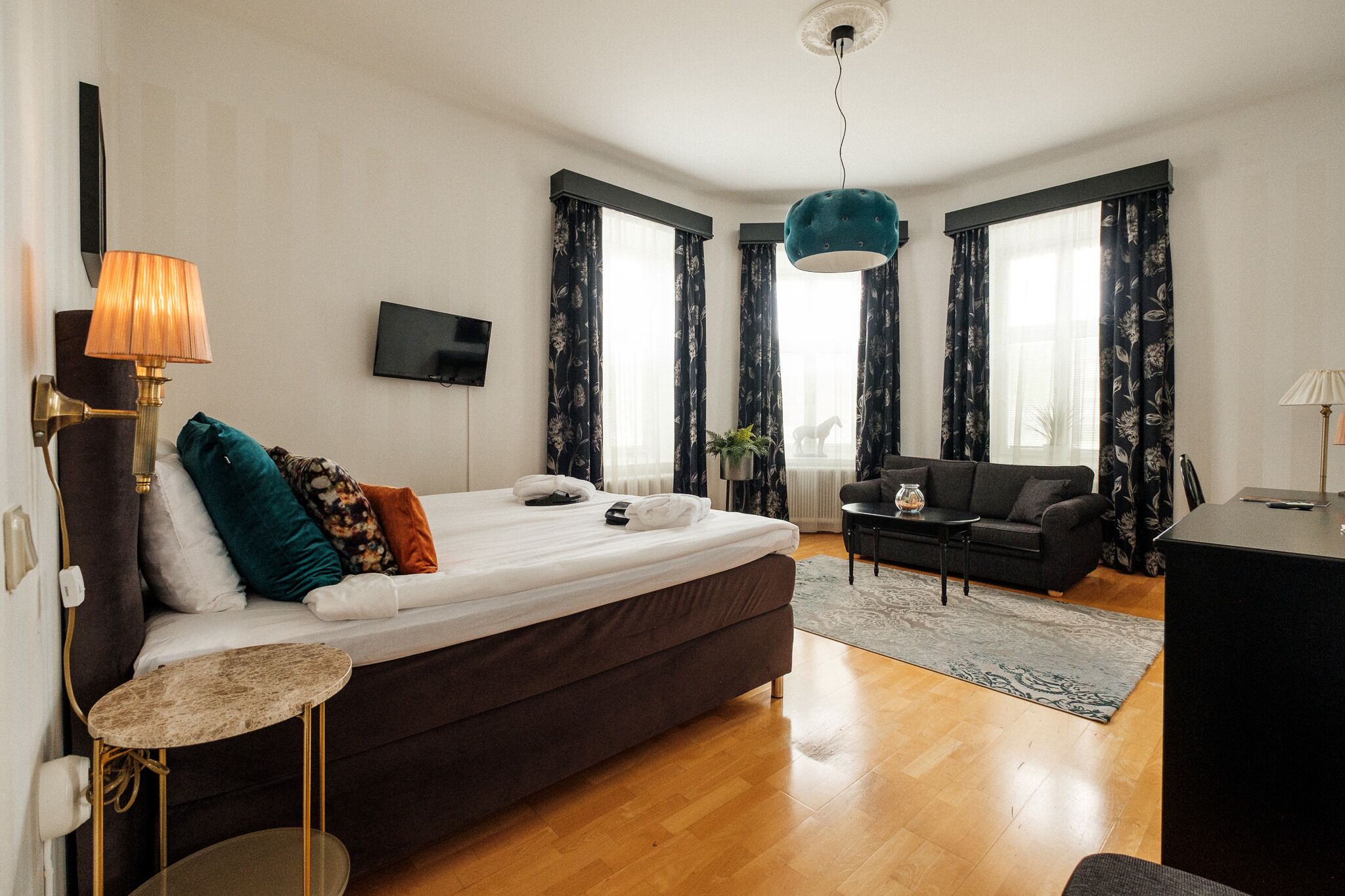 A modern bedroom with a large bed, a small table, a sofa, and a TV on the wall.