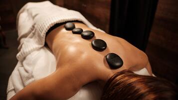Une personne reçoit un massage du dos avec des pierres noires disposées le long de la colonne vertébrale.