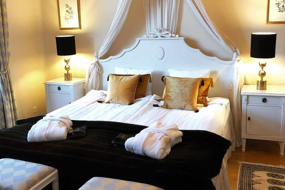 Un dormitorio ordenado con cama con dosel, mesitas de noche con lámparas y un candelabro.