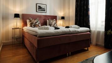 Uma cama bem arrumada com cabeceira vermelha, duas luminárias de apoio e um quadro na parede.