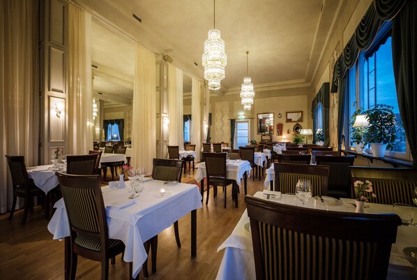 Comedor con mesas dispuestas para el servicio, candelabros y ventanas amplias con cortinas.