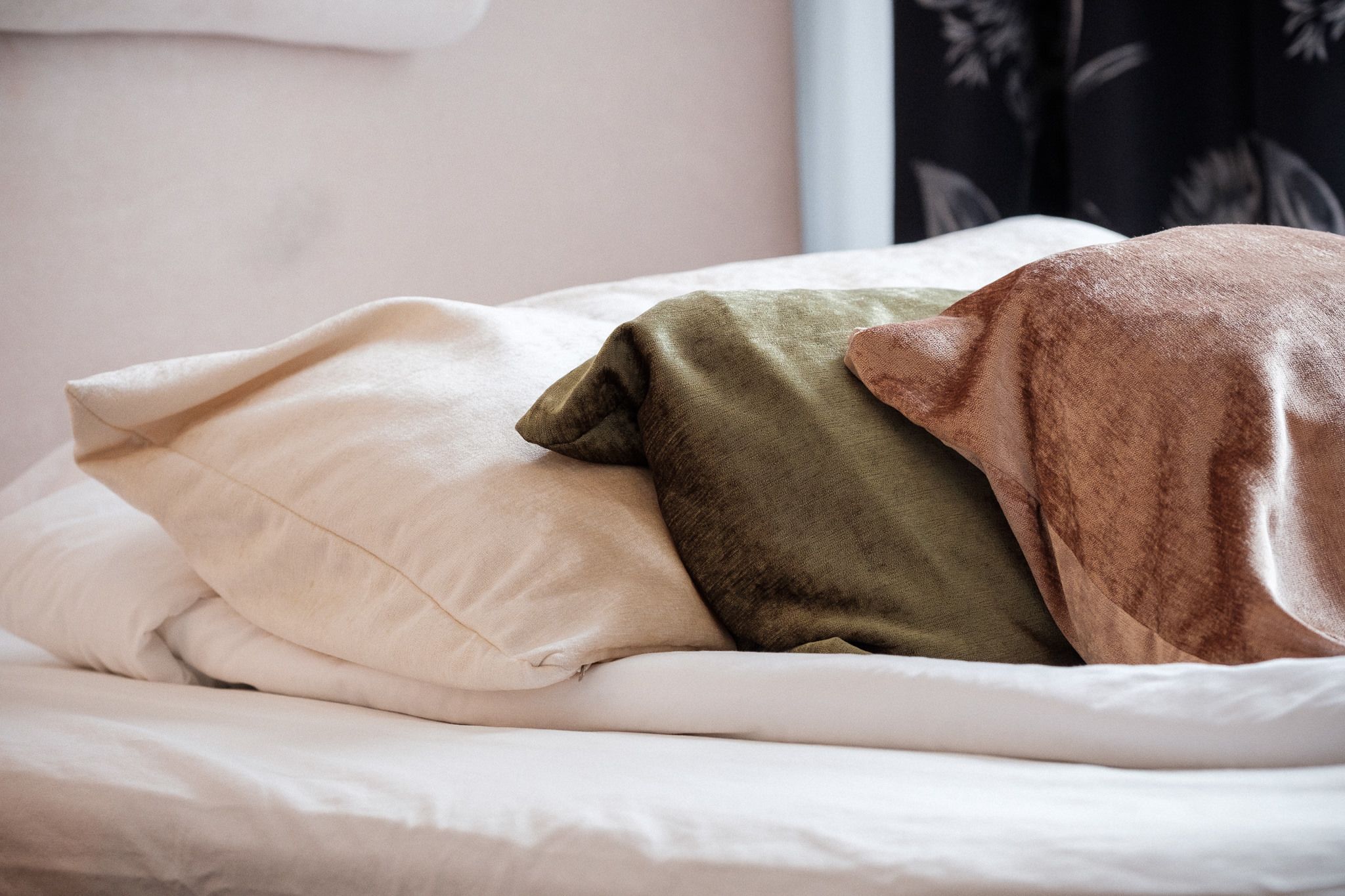 A bed with three pillows in different colors.