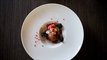 A dessert on a white plate with berries and mint on a dark wooden table.