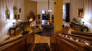 Una imponente escalera conduce a una sala de estar con chimenea, sofás y una araña.