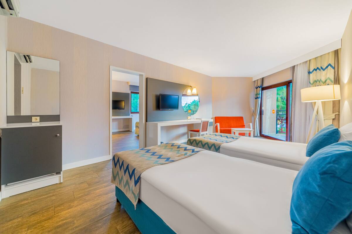 Habitación de hotel con dos camas, un escritorio con silla, un televisor y una ventana con cortinas.