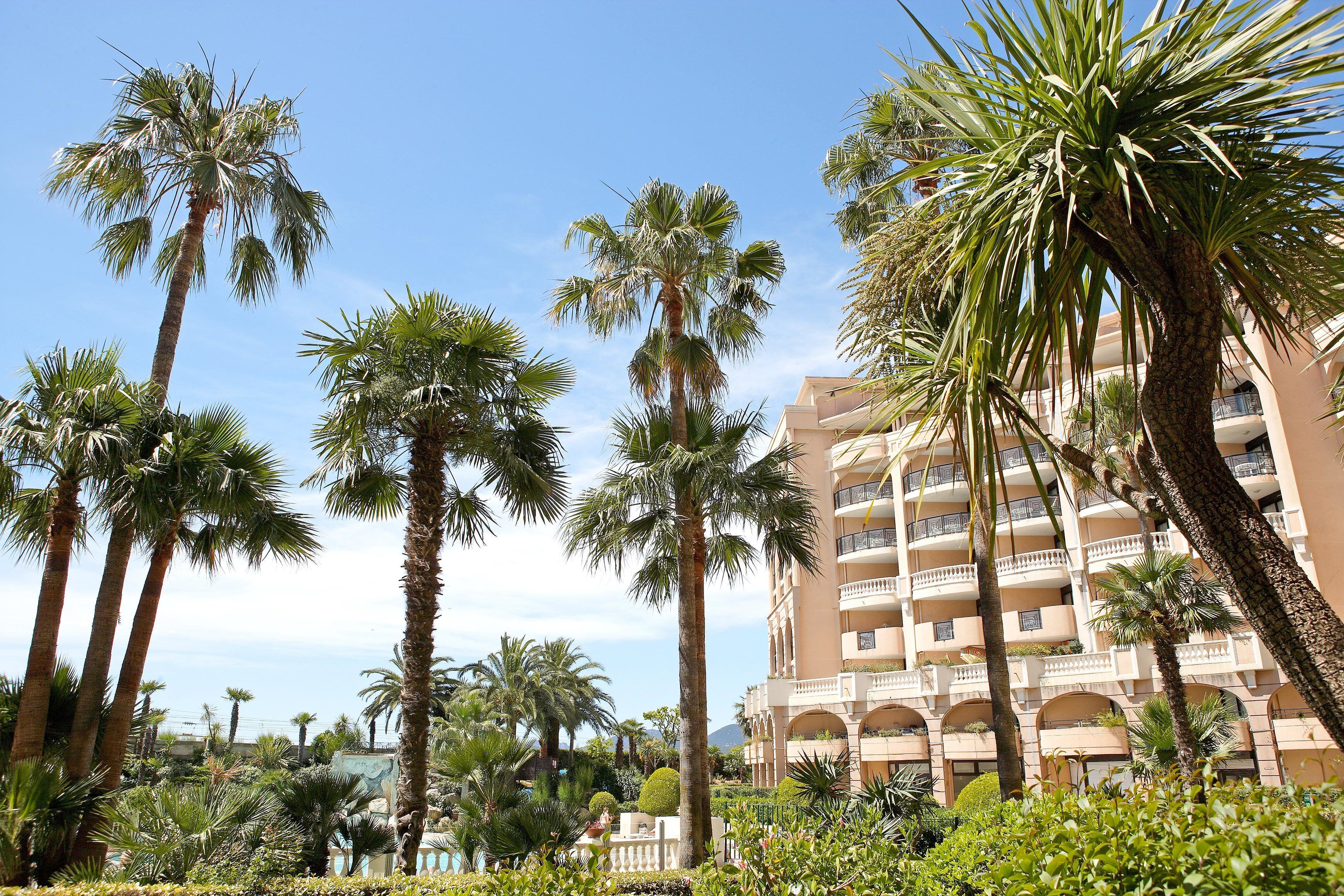 A hotel with multiple floors, palm trees, and a clear blue sky.