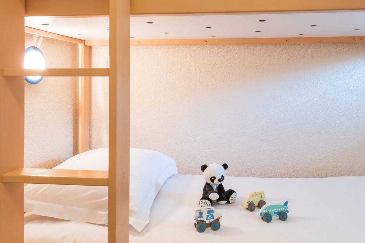 Una cama litera con escalera, un pequeño osito panda de juguete y vehículos de juguete en la cama inferior.