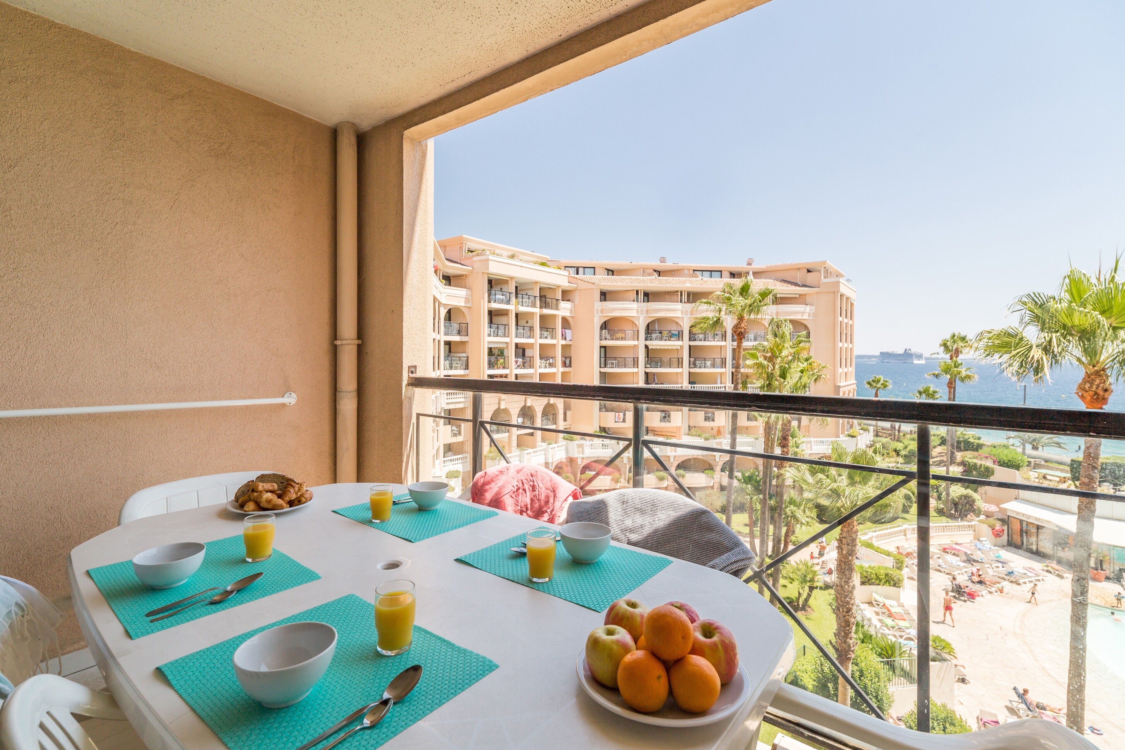 En balkon med et spisebord dækket til morgenmad, med udsigt over en pool og en bygning.