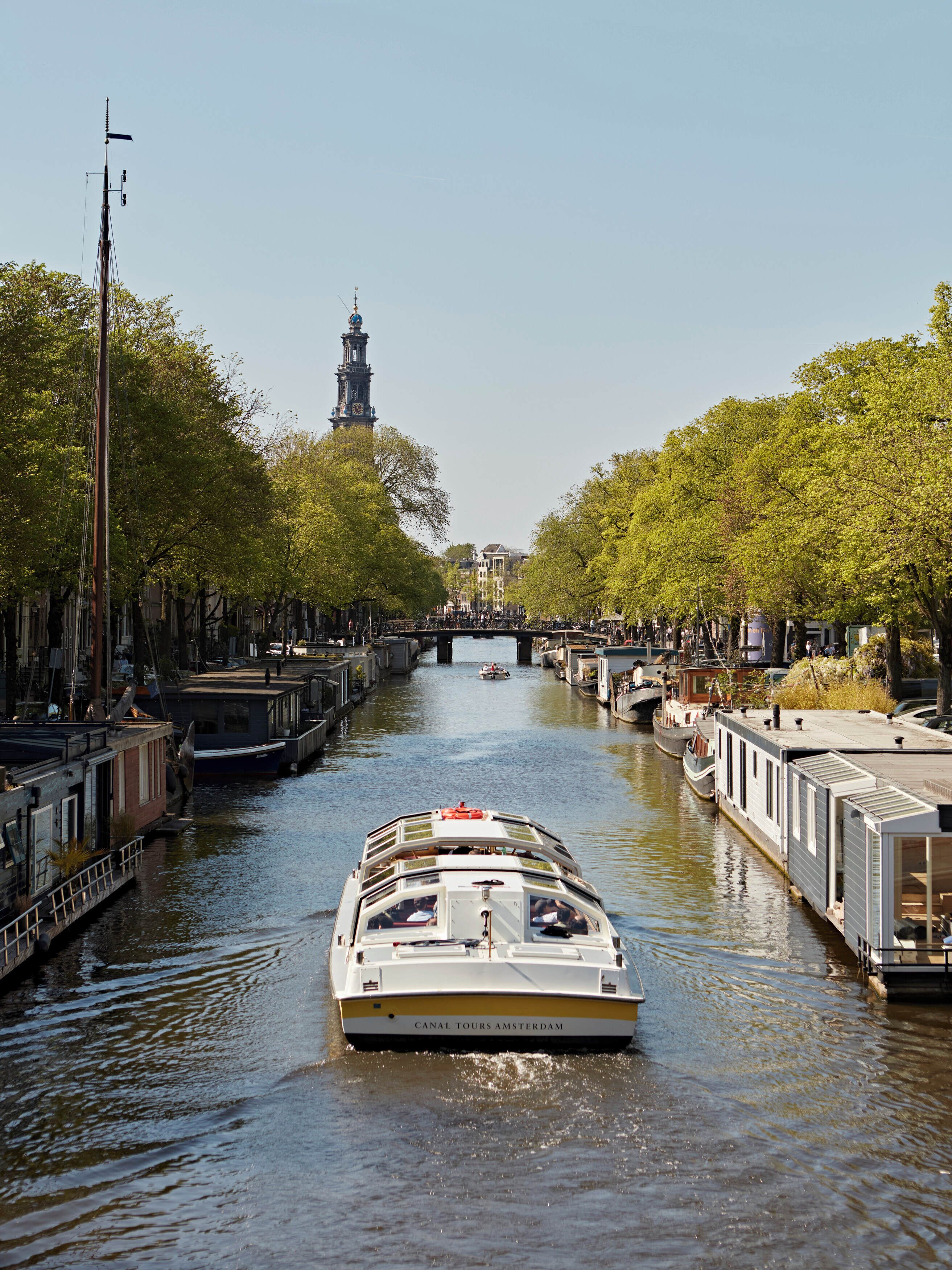 A canal tour boat moving through a waterway flanked by trees and buildings.