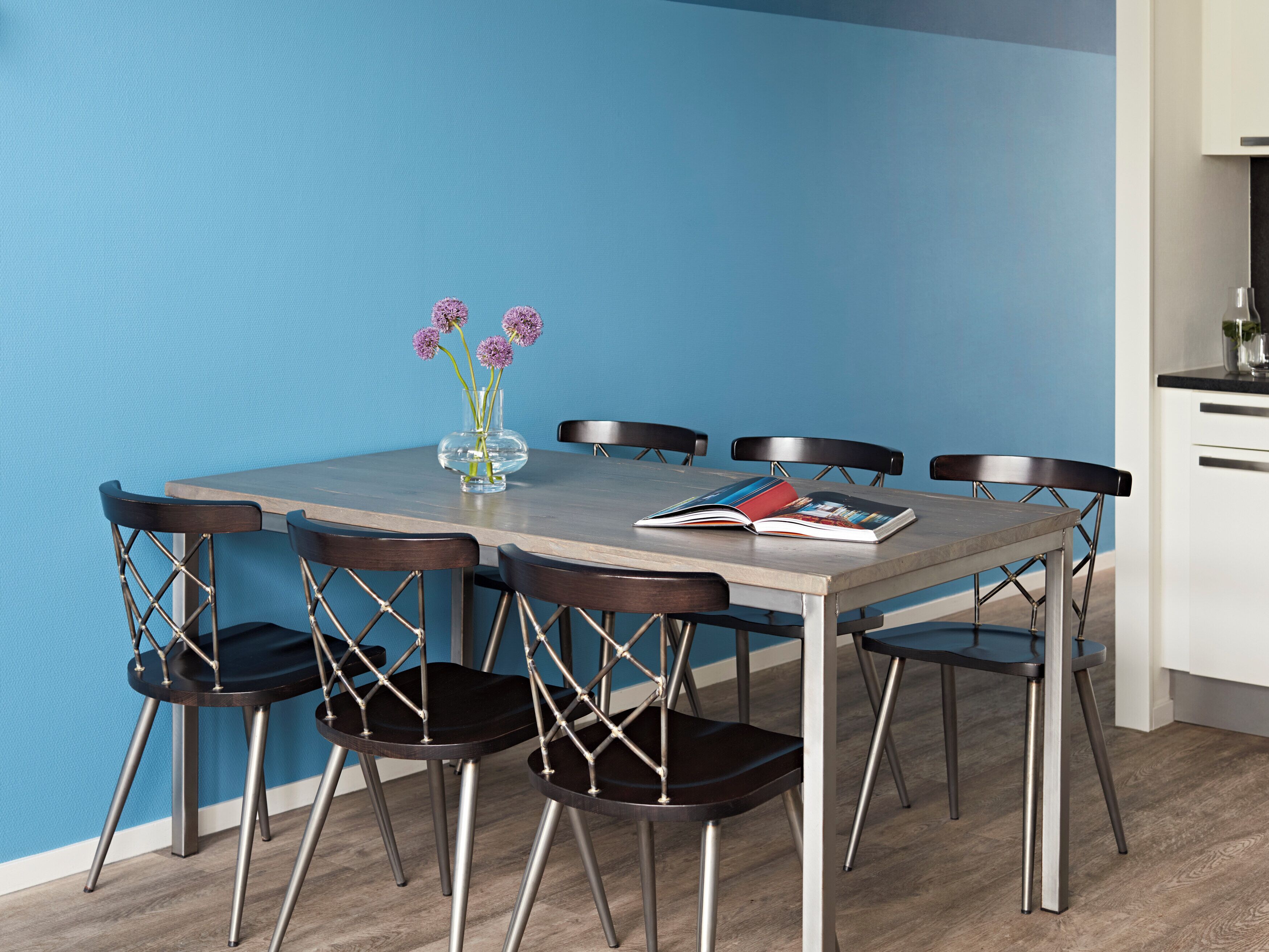 A dining table with six chairs, a vase with flowers, and a magazine.