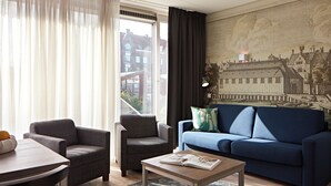 A modern living room with a blue sofa, two armchairs, a coffee table, and a cityscape mural on the wall. - YAYS Amsterdam Prince Island by Numa (Amsterdam)