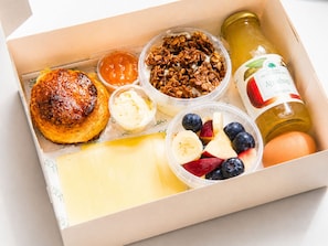 Une boîte de petit-déjeuner contenant un croissant, du granola, un yaourt, des fruits, du fromage et une bouteille de vinaigre de cidre de pomme.