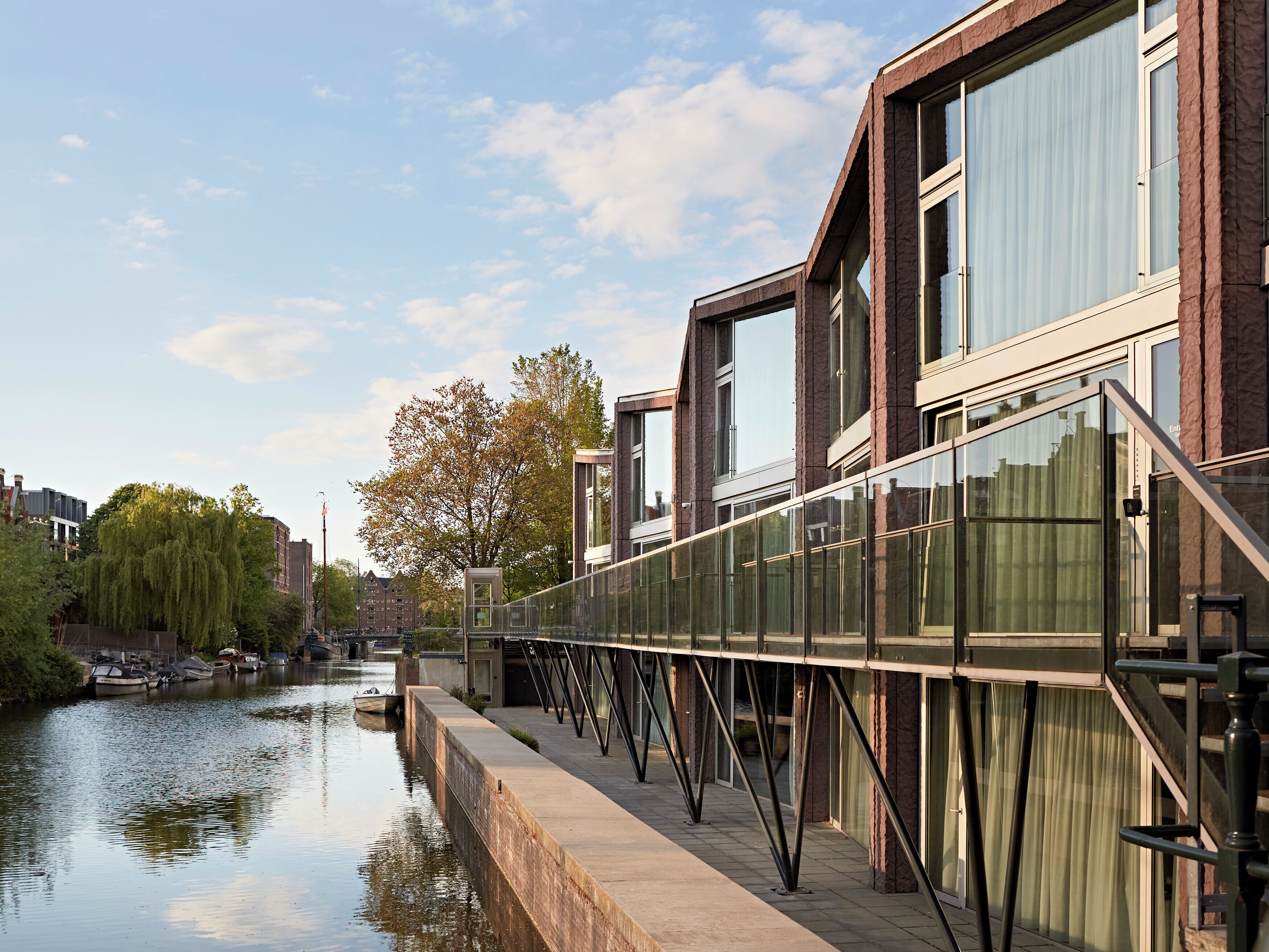 Een modern gebouw met grote ramen en een glazen brug over een gracht.