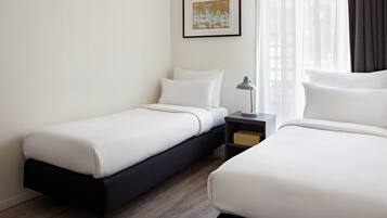 A hotel room with two single beds, a nightstand with a lamp, a framed picture on the wall, and a window with curtains.