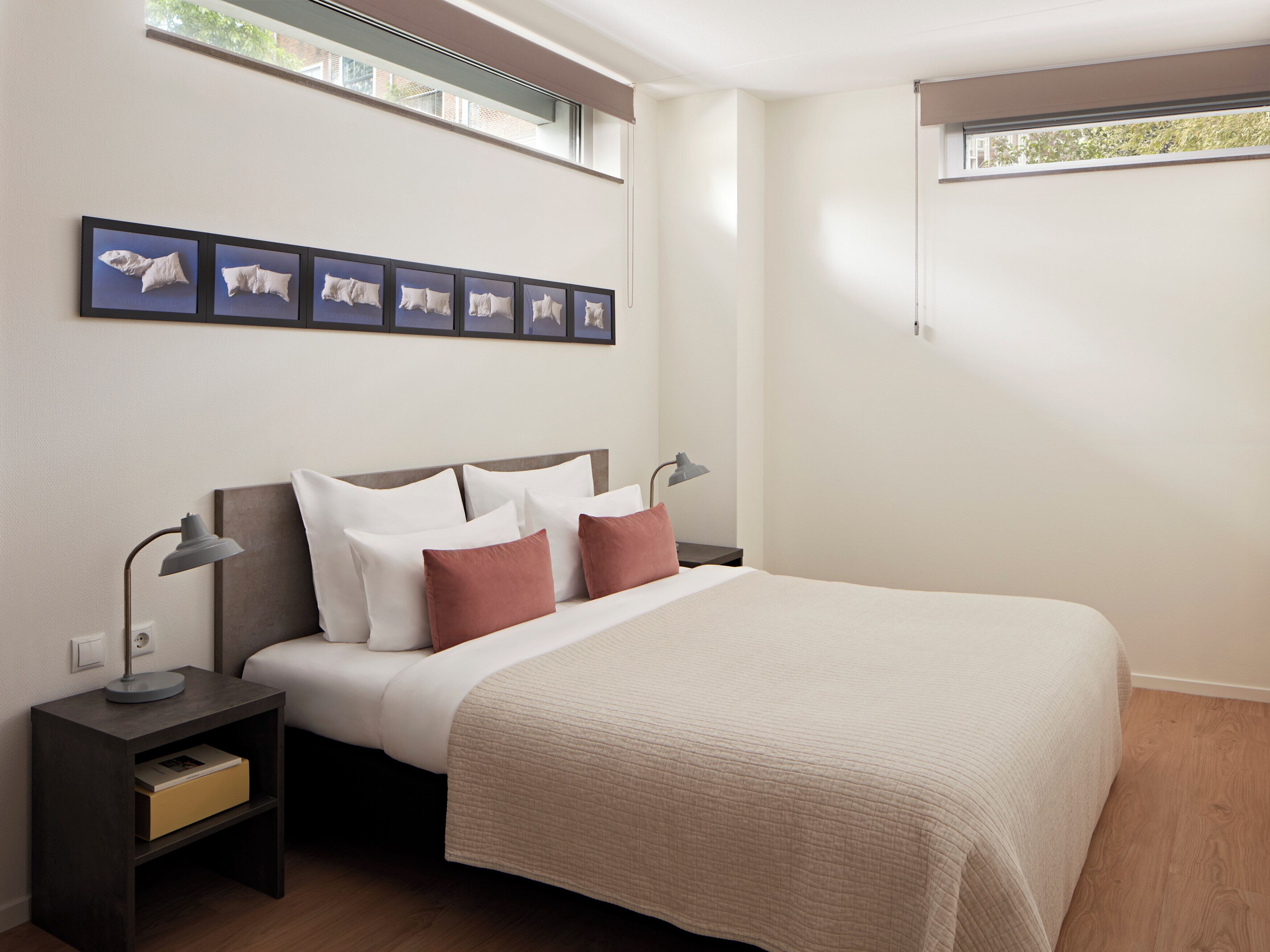 Un dormitorio con cama, mesitas de noche, lámpara, ventana y decoración en la pared.
