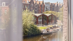 A canal with boats, a modern building with large windows, and traditional brick houses in the background. - YAYS Amsterdam Prince Island by Numa (Amsterdam)