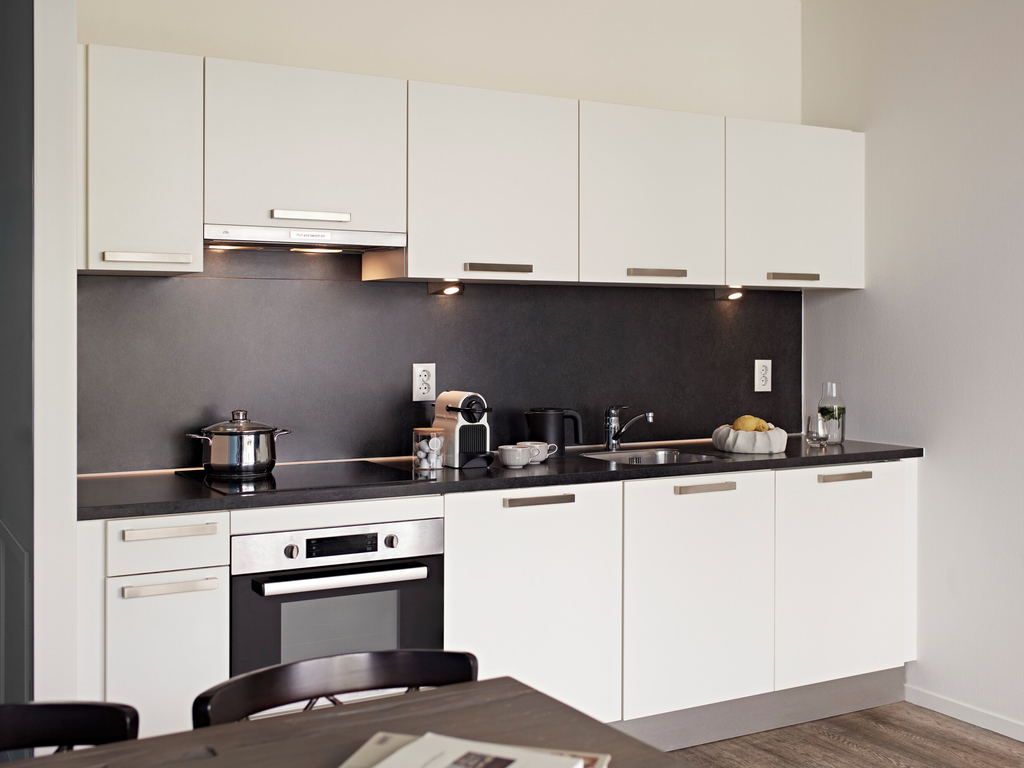 A modern kitchen with white cabinets, a black countertop, a built-in oven, and a sink.