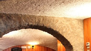 Un restaurante con paredes de madera y arcos de piedra, con mesas cubiertas de manteles escoceses y sillas.
