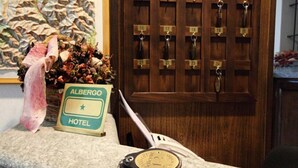 Una recepción con un letrero que dice "Albergo Hotel", un reloj y una puerta con llaves numeradas.