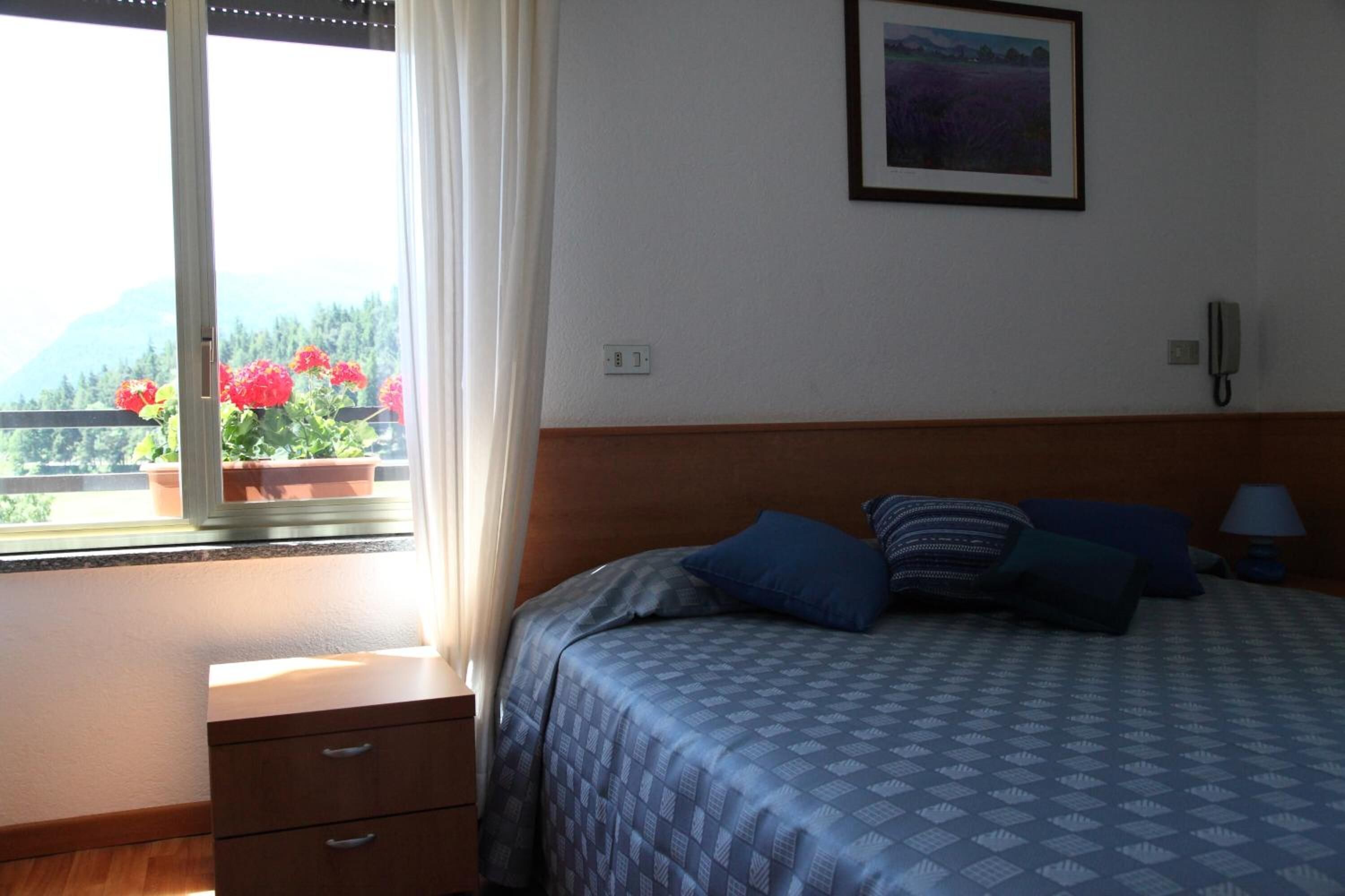 A bedroom with a bed, a nightstand, a telephone, a window with curtains, and a framed picture on the wall.