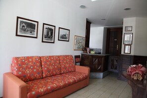 A living room with a red patterned sofa, a wooden cabinet, and three framed pictures on the wall. - Hôtel Bellavista (Saint-Nicolas)