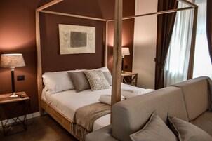 Une chambre à coucher avec un lit à baldaquin, une table de chevet avec une lampe, une petite table avec une lampe et une grande fenêtre avec des rideaux.