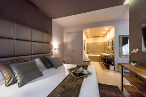 Une chambre d’hôtel moderne avec un grand lit, une table de chevet, un plateau avec des articles pour le petit-déjeuner et une salle de bain équipée d’un lavabo et d’un miroir.