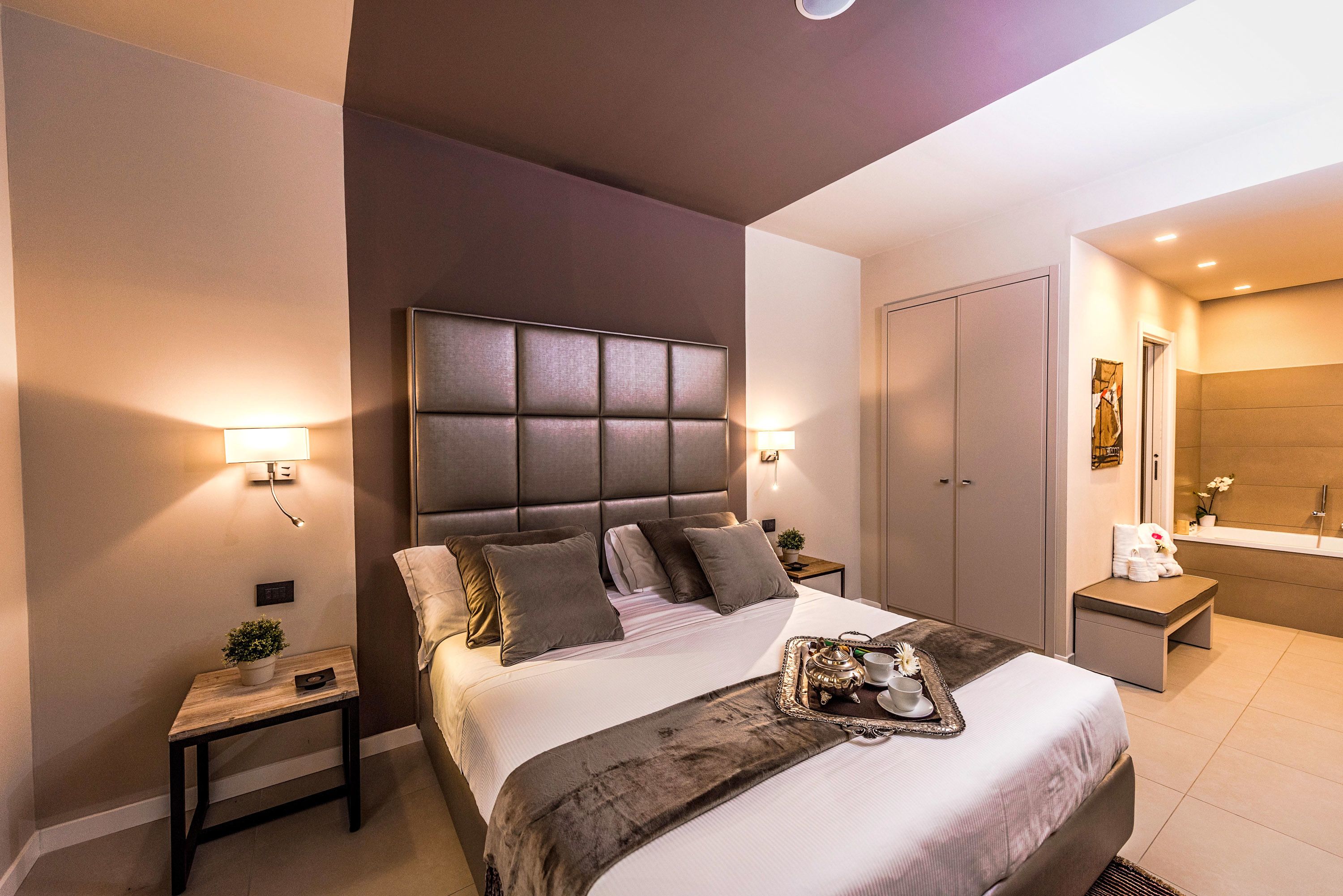 Una habitación de hotel moderna con una cama grande, mesitas de noche, un baño con bañera y un espejo.