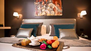 Una cama bien hecha con una bandeja de desayuno que incluye cruasanes, fruta y una rosa.