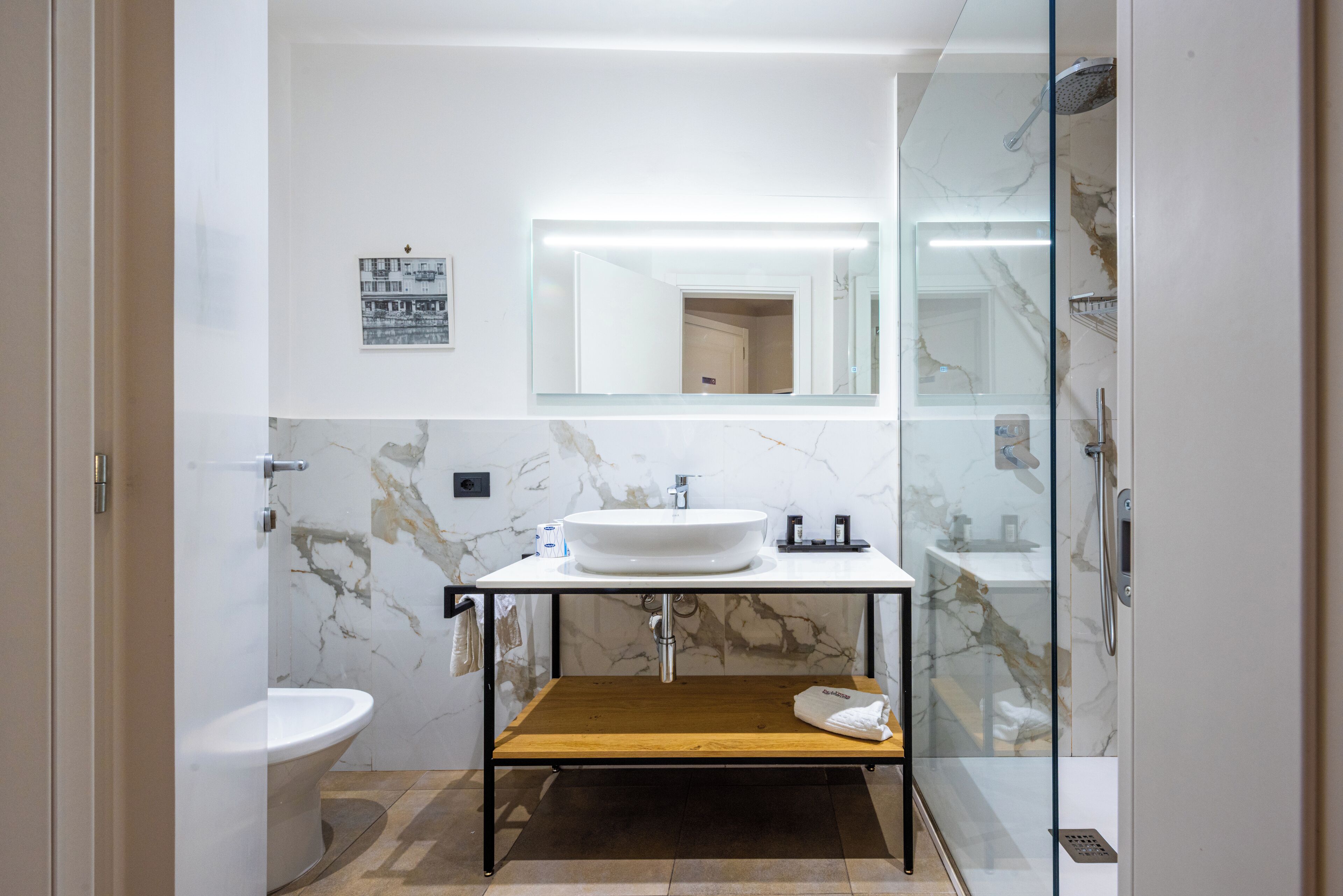 A modern bathroom with a marble vanity, a glass shower enclosure, and a wooden shelf.