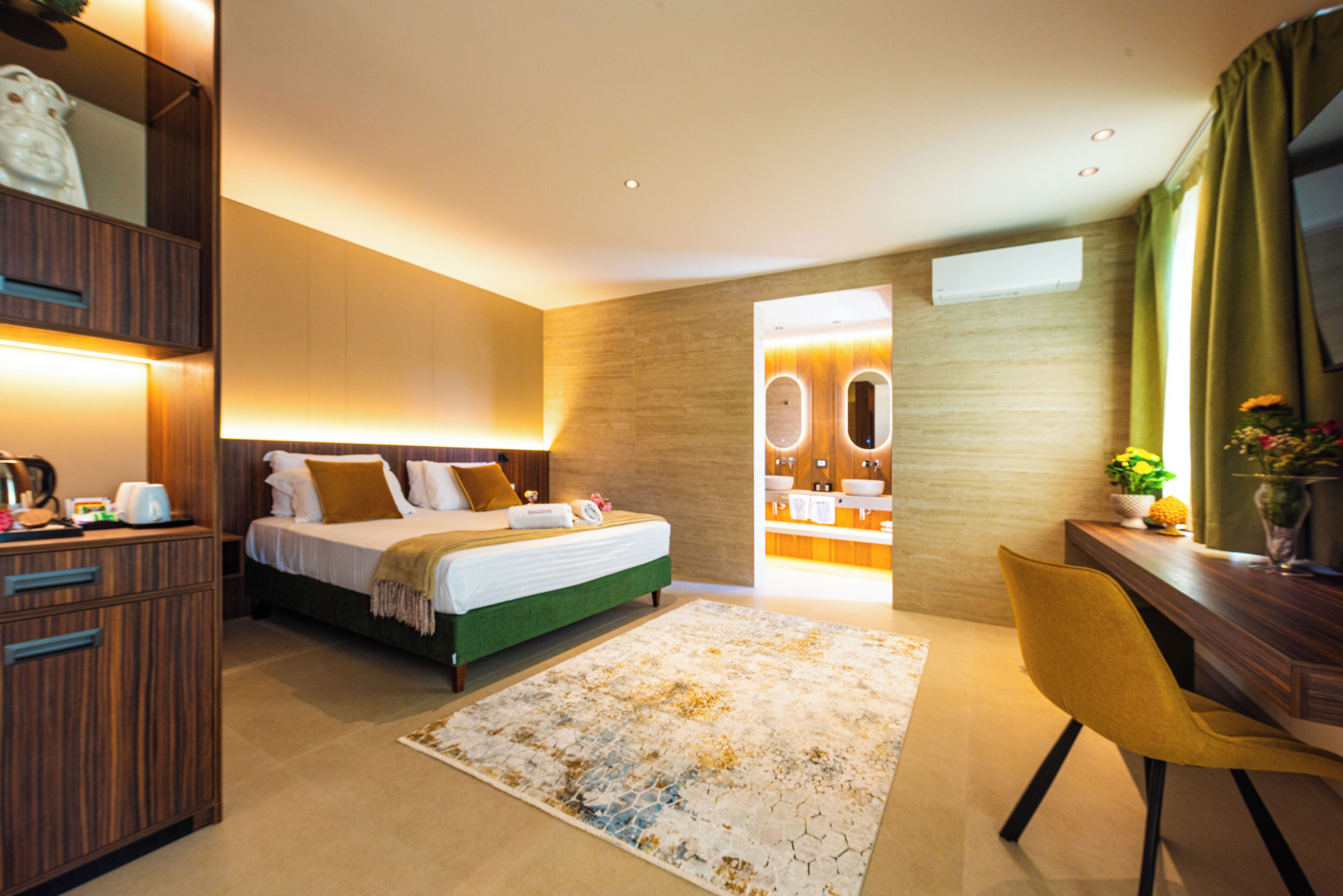 Una camera d'albergo moderna con un letto, una scrivania, una sedia e un bagno visibile attraverso una porta aperta.