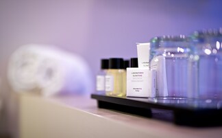 Un ripiano con diversi articoli da toilette, tra cui una bottiglia etichettata “LABORATORIO OLFATIVO” e altri prodotti per la cura personale.