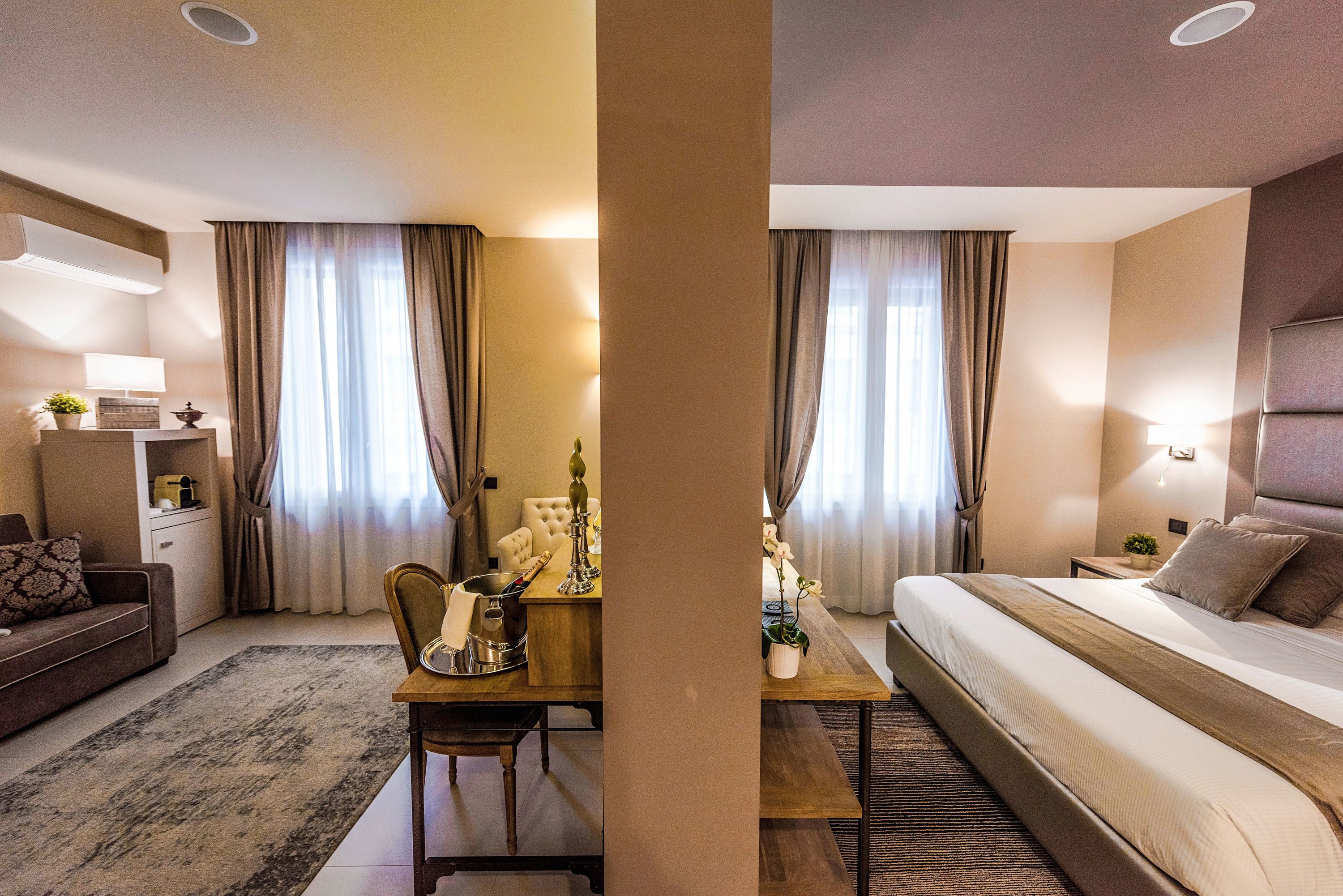 Ein Hotelzimmer mit Bett, Schreibtisch mit Stuhl, einer Couch und einem Nachttisch mit Lampe.